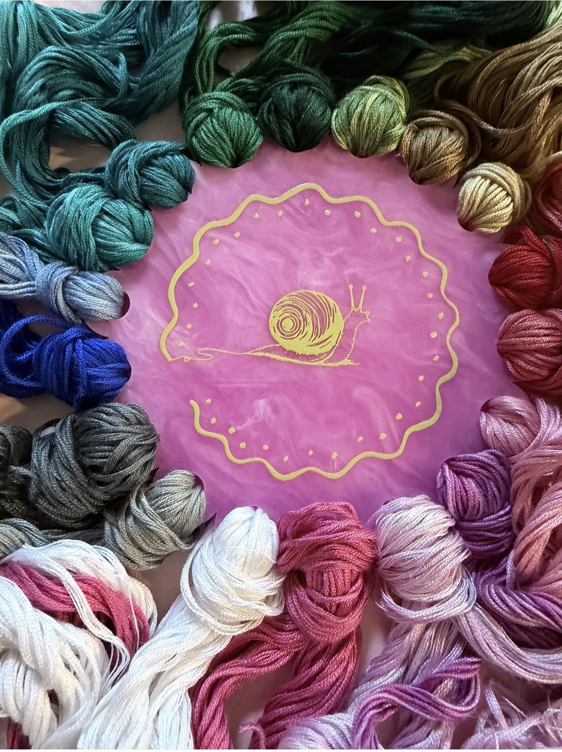 A rainbow of hand-dyed silk embroidery threads circling the Silk Snail badge